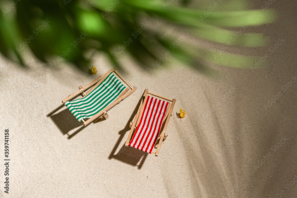 Aerial view two deck chair, glass of juice, flip flops on sand through the branches of palm and shadow palm tree. Travel, holiday, summertime, romantic concept. Top view. Aerial view two deck chair, glass of juice, flip flops on sand through the branches of palm and shadow palm tree. Travel, holiday, summertime, romantic concept. Top view.
