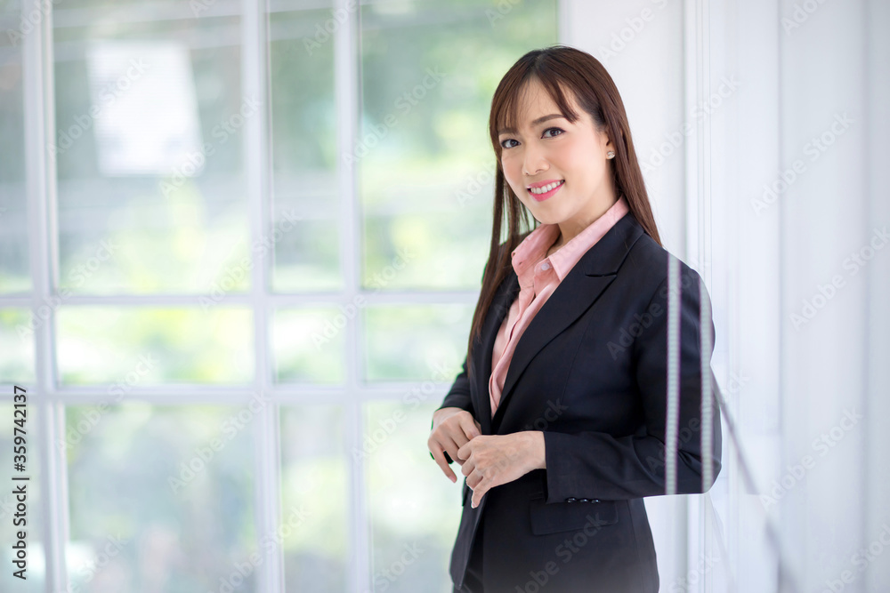 Beautiful Asian businesswomen wearing a black suit standing in the office, smiling confidently and looking at the camera. Asian business women concept Beautiful Asian businesswomen wearing a black suit standing in the office, smiling confidently and looking at the camera. Asian business women concept