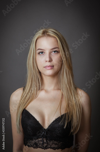 a young woman in a black bra poses against a dark wall