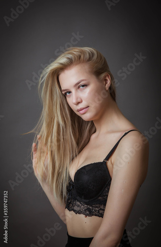 a young woman in a black bra poses against a dark wall