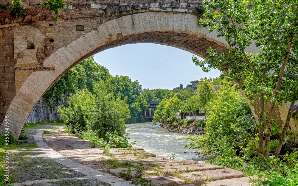 trees and plants near a perfect arch of an ancient bridge over Tiber river, Rome Italy