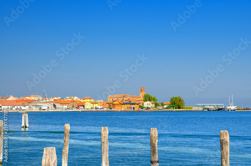 Panoramic view of Lusenzo lagoon with wooden poles in water and Chioggia town cityscape with Saint Domenico catholic church and old buildings in historical centre, blue sky, Veneto Region, Italy © Aliaksandr