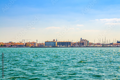 Panoramic view from sea lagoon of Chioggia town cityscape with port and old buildings in historical centre, blue sky background in summer day, Veneto Region, Northern Italy © Aliaksandr