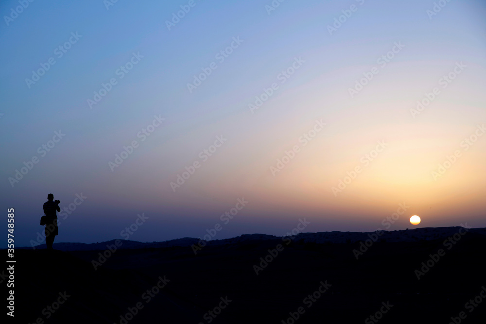 silhouette of a man taking photo in Dubai desert at sunset