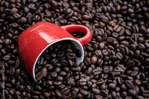 red coffee cup filled and surrounded by black coffee beans