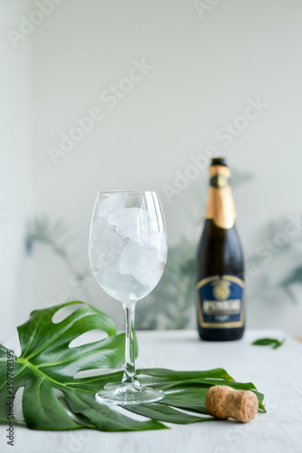 Sparkling wine with ice in glass standing on the green mostera leaf on the white table and champagne bottle