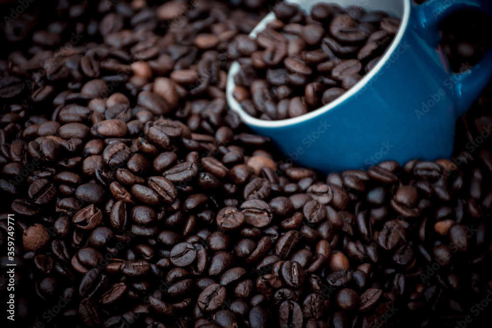 blue coffee cup filled with black coffee beans and surrounded by them blue coffee cup filled with black coffee beans and surrounded by them