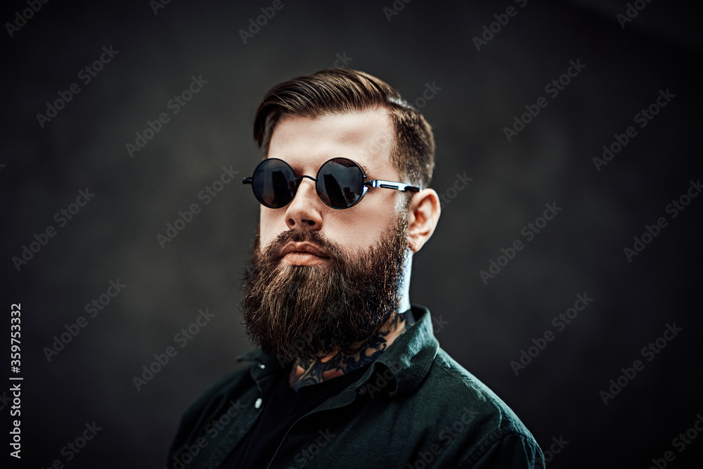 Closeup portrait of a cool bearded male in sunglasses on a dark background