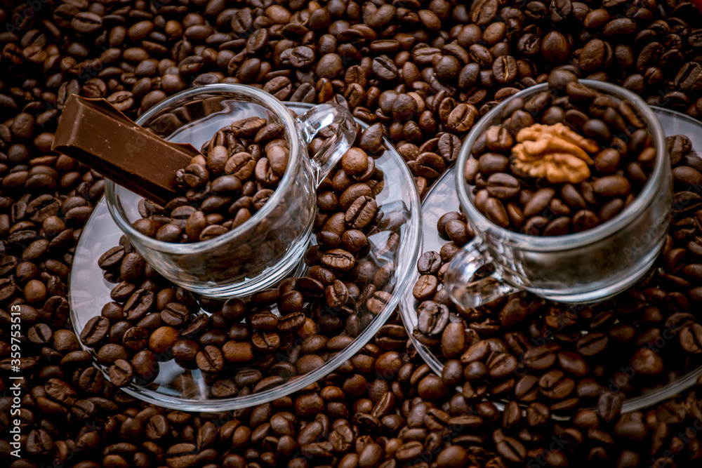 Fototapeta premium Coffee cups with saucers surrounded and filled with coffee beans, one with a chocolate bar and the other with a walnut