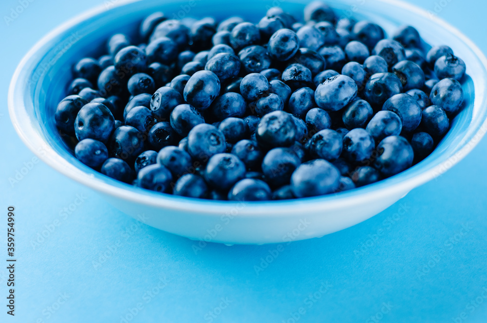 Blueberries in a bowl on a wooden table. Top view of plate and blueberries on violet surface Blueberries in a bowl on a wooden table. Top view of plate and blueberries on violet surface