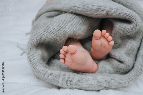 A small child sleeps on a white bed, covered with a gray plaid close-up. The legs of the newborn. Photography, concept.