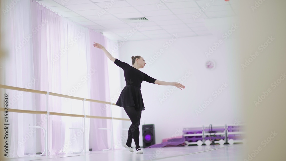 Fototapeta premium A professional ballerina in a black pack dances in a large training hall