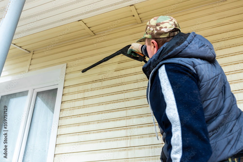 Fototapeta premium Cleaning the vinyl siding wall with a high-pressure washer.