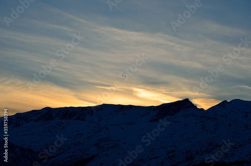 paraglider over snow covered mountain with bright and colourful dawn light in the arctic circle