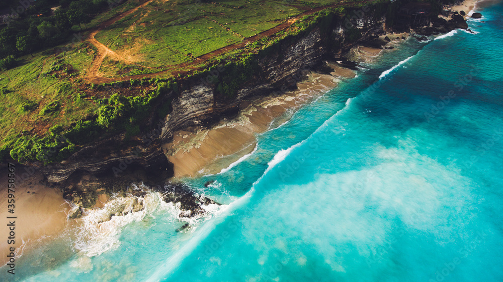 Aerial photo from flying drone of an amazing nature scenery with rock cliff on sandy coastline. Beautiful sea water with waves for surfing in summer season in Bali. Beauty Indian ocean landscape