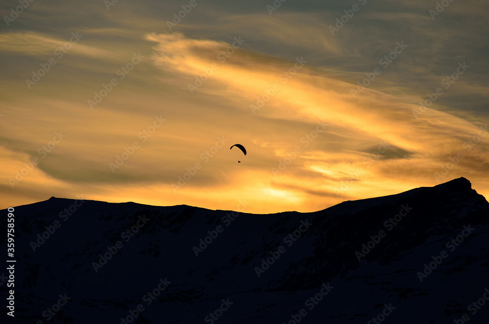 Paraglider on vibrant colourful dawn sky with majestic snow covered mountain underneath in the arctic circle