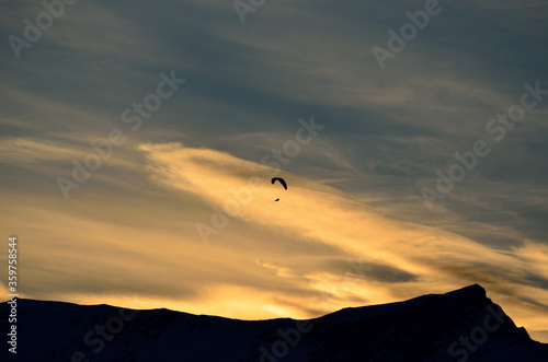 paraglider on a vibrant and bright dawn sky flying over majestic snow covered mountain top in the arctic circle