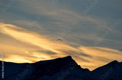 Paraglider on vibrant colourful dawn sky with majestic snow covered mountain underneath in the arctic circle