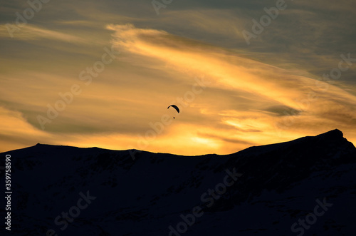 Paraglider on vibrant colourful dawn sky with majestic snow covered mountain underneath in the arctic circle