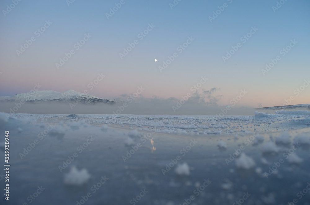 ice fog over fjord with thick ice, moonlight and colorful pink sunset sky