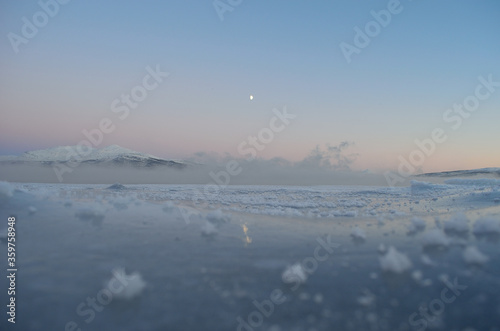 ice fog over fjord with thick ice, moonlight and colorful pink sunset sky
