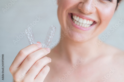 Close-up of orthodontic silicone transparent teeth aligner in female hands. A woman with a perfect charm smile holds a removable night retainer. Bracket for teeth whitening. Cropped photo. photo