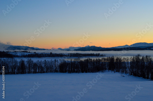 ice fog over calm fjord with strong colorful sunset sky and snowy mountain range in winter © Arcticphotoworks