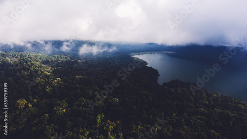 Aerial photo from flying drone of a beautiful nature landscape with green tropical forest near lake in gloomy weather. Amazing wilderness view and sky with thunderclouds. Vintage noise effect