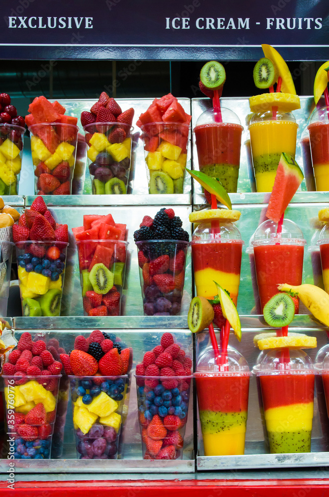 Fototapeta premium A lot of transparent plastic glasses filled with fresh fruits, prepared for the manufacture of natural juices and cocktails, fresh juices in plastic glasses. Organic drinks and foods. Takeaway fruits