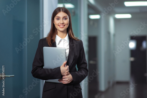 Happy Beautiful Business Woman in Office Hall with a laptop in his hands.