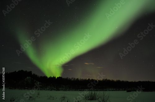 incredible strong aurora borealis over snowy mountain and frozen river bed in winter landscape