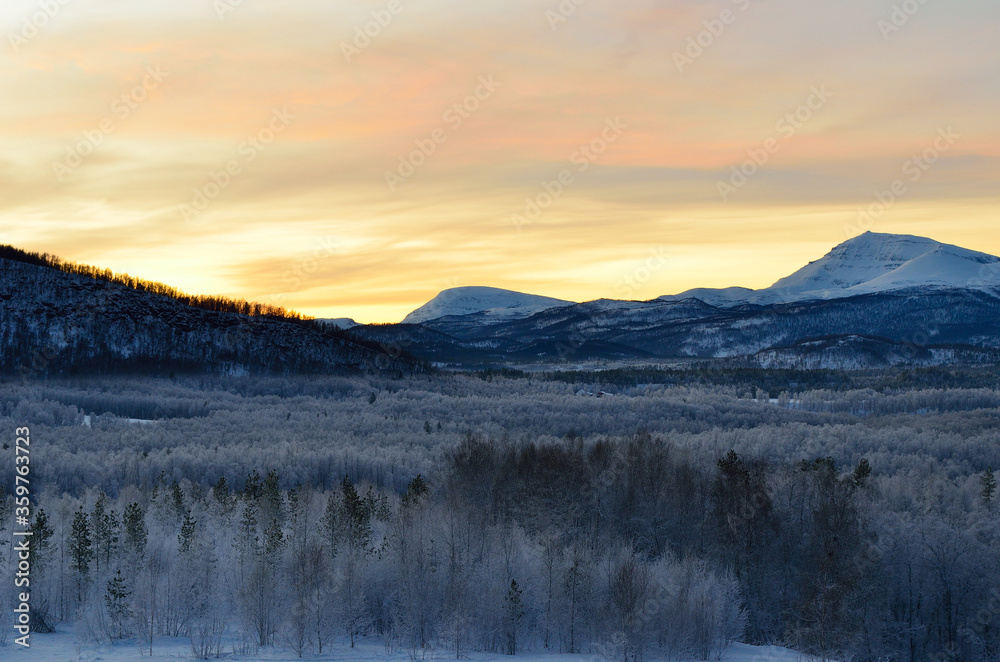 Scenic snowy mountain with vibrant colourful sky and white frost covered forest in the front