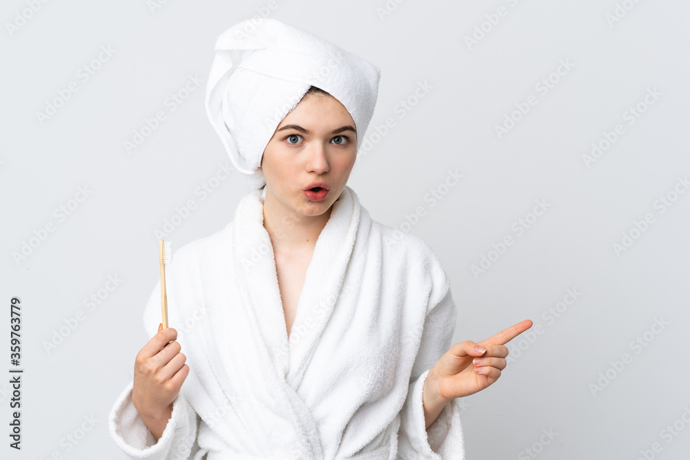 Young woman in a bathrobe holding toothbrush surprised and pointing side Young woman in a bathrobe holding toothbrush surprised and pointing side