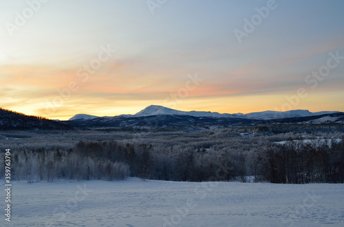 Scenic snowy mountain with vibrant colourful sky and white frost covered forest in the front