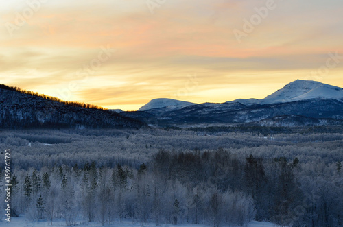 Scenic snowy mountain with vibrant colourful sky and white frost covered forest in the front