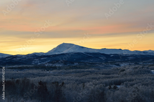 Scenic snowy mountain with vibrant colourful sky and white frost covered forest in the front