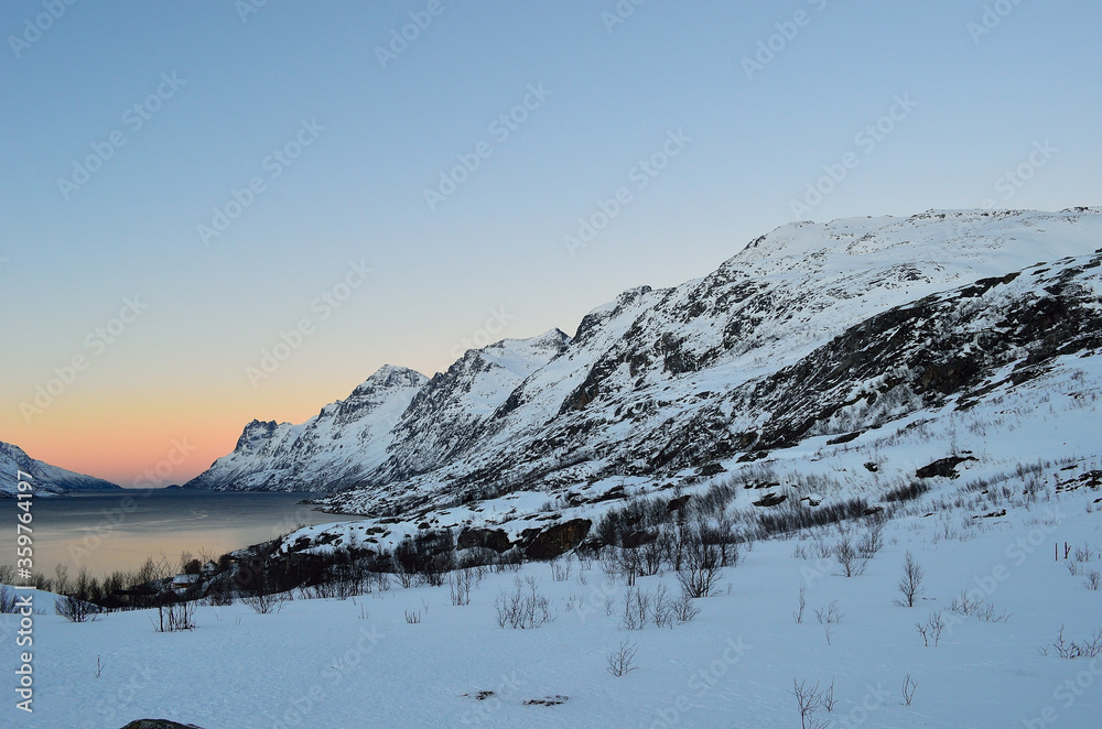 Naklejka premium High snow covered mountain surround fjord with vibrant dawn sky in the winter