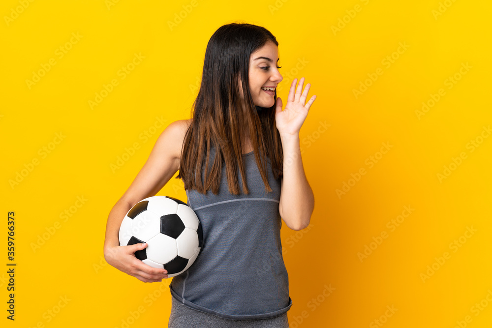 Young football player woman isolated on yellow background shouting with mouth wide open to the side Young football player woman isolated on yellow background shouting with mouth wide open to the side