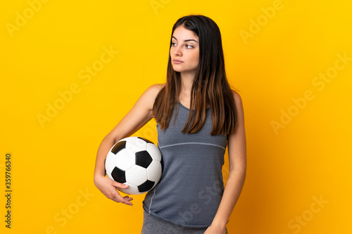 Young football player woman isolated on yellow background looking to the side © luismolinero