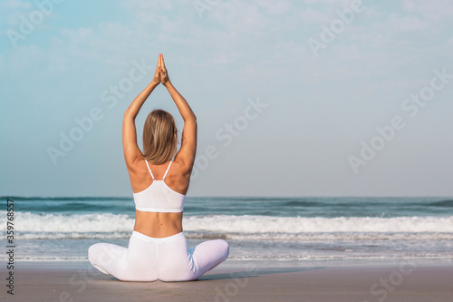 a beautiful girl in white clothes is sitting on the ocean and practicing yoga and meditation