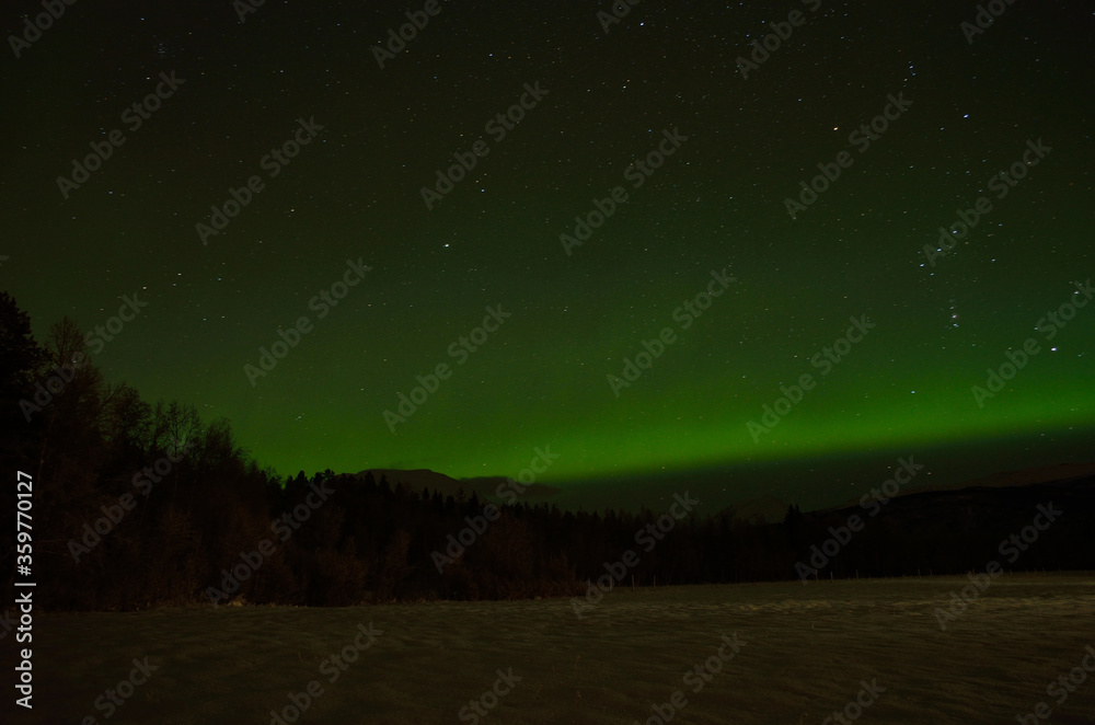 strong aurora borealis over snowy mountains and field in winter night