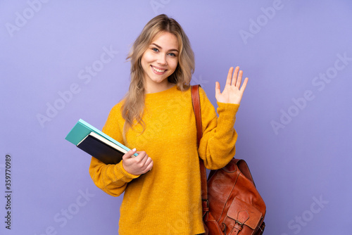 Teenager Russian student girl isolated on purple background saluting with hand with happy expression