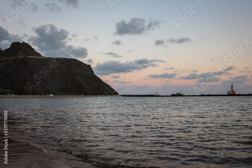 A beach at sunset with a ship in the background and hillside on the left