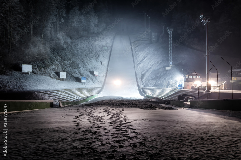 Ski jump at night illuminated by lights covered with snow. Winter sport season. Wide shot, looking up - obrazy, fototapety, plakaty 