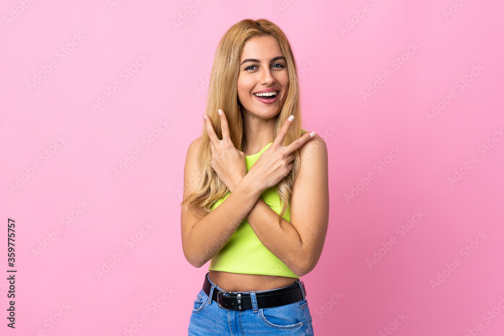 Young Uruguayan blonde woman over isolated pink background smiling and showing victory sign