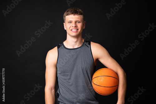 Handsome young man playing basketball over isolated black wall © luismolinero