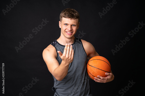 Handsome young man playing basketball over isolated black wall © luismolinero