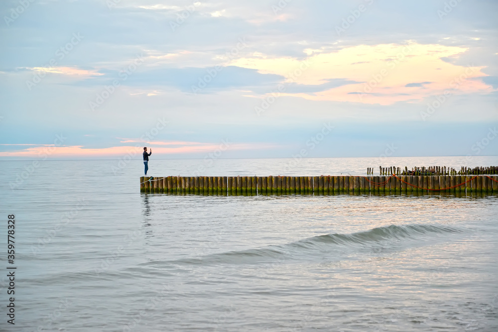 A man stands on a wave and takes a selfie in the summer evening. Baltic sea. Zelenogradsk, Kaliningrad region