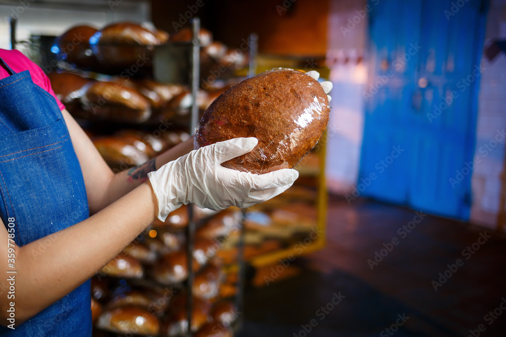 A worker works in a bakery. She puts bread on a shelf. Fresh crispy bread close-up
