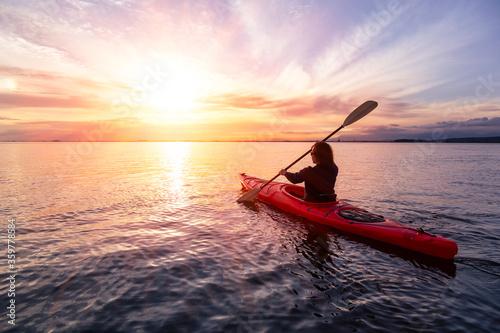Sea Kayaking in calm waters during a colorful and vibrant sunset. Adventure Girl in Red Kayak. Location: White Rock, Vancouver, British Columbia, Canada. © edb3_16